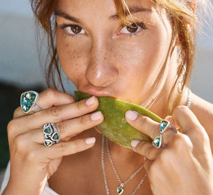 Woman biting into a green fruit with turquoise gemstone rings on her fingers.