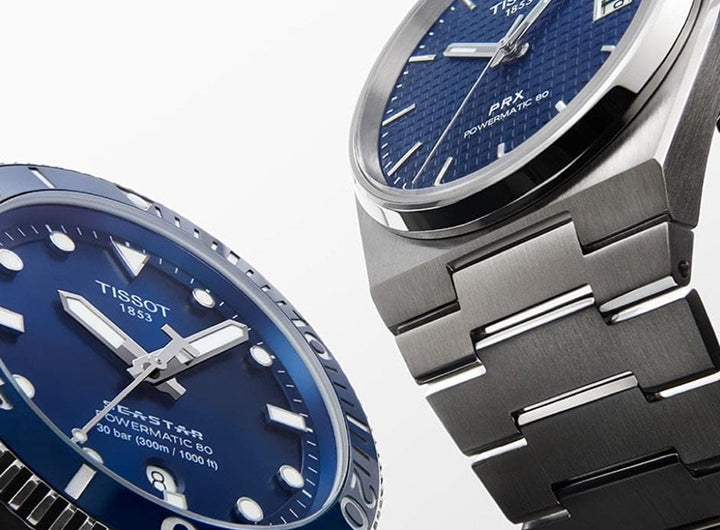 Two Tissot watches with blue faces and silver metal bands on a white background
